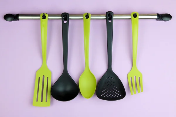 Plastic kitchen utensils on silver hooks on lilac background — Stock Photo, Image