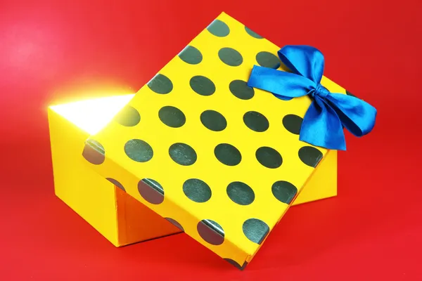 Gift box with bright light on it on red background — Stock Photo, Image