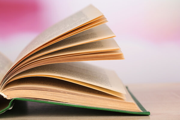 Открытая книга на деревянном столе на ярком фоне
