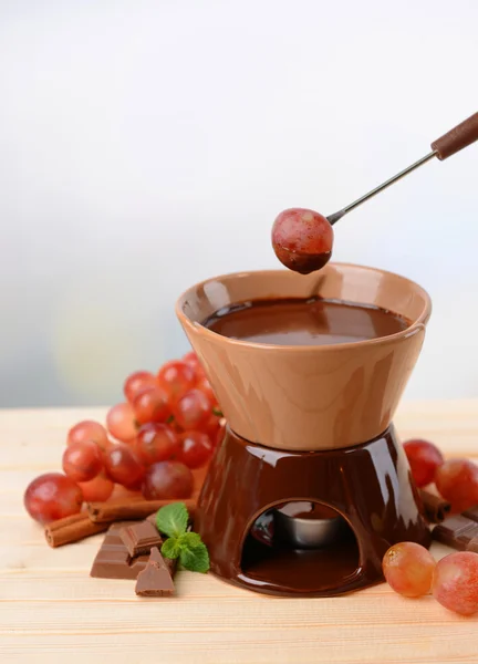 Chocolate fondue with fruits, on wooden table, on light background — Stock Photo, Image