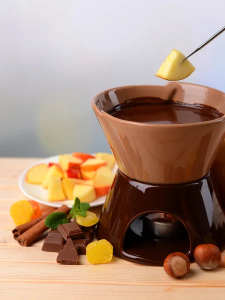 Chocolade fondue met fruit, op houten tafel, op lichte achtergrond — Stockfoto