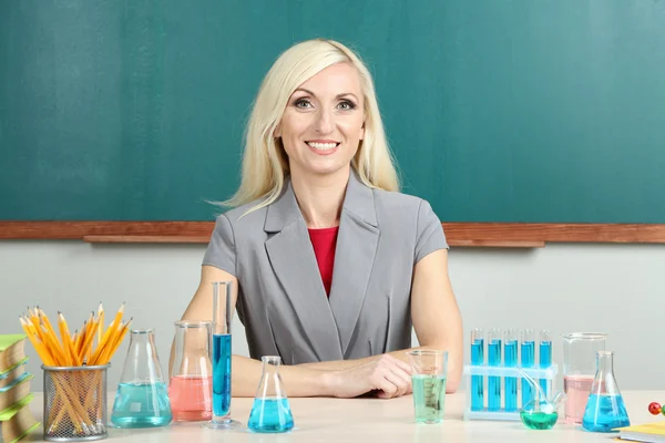 Učitel chemie, sedící u stolu na tabuli pozadí — Stock fotografie