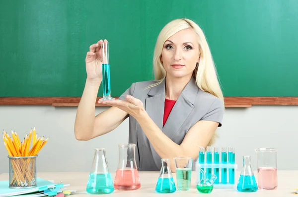 Profesor de química con tubos sentado en la mesa sobre fondo de pizarra — Stock fotografie