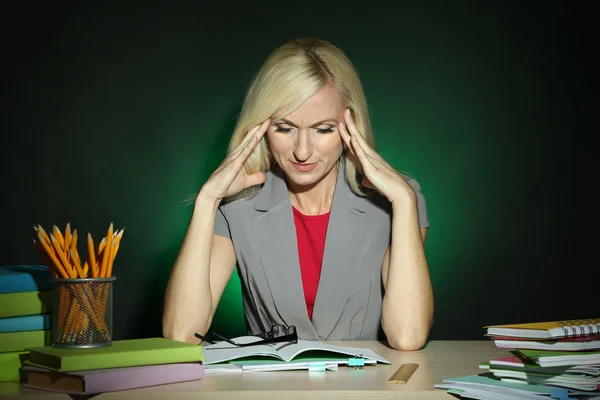 Moe leraar zittend aan tafel op donkere kleurrijke achtergrond — Stockfoto