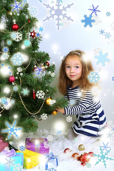 Маленькая девочка украшает елку безделушками в комнате — стоковое фото