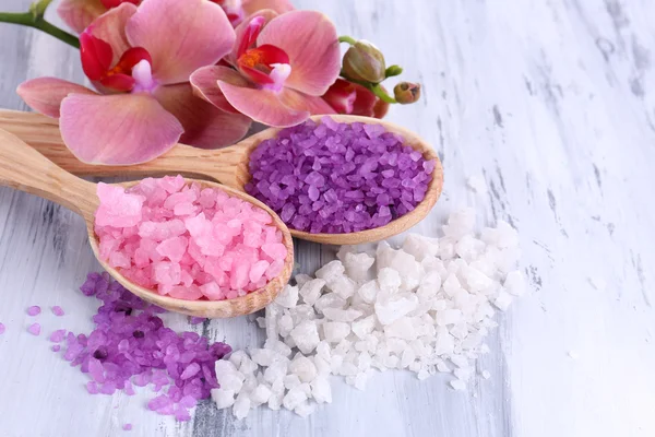 Bodegón con hermosa flor de orquídea y cucharas de madera con sal marina, sobre fondo de madera de color —  Fotos de Stock