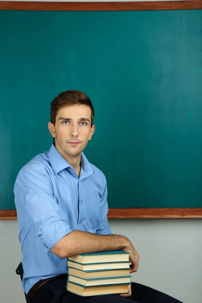 Unga lärare sitter nära svarta tavlan i skolan klassrum — Stockfoto