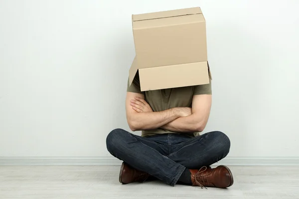 Человек с картонной коробкой на голове сидит на полу возле стены — стоковое фото