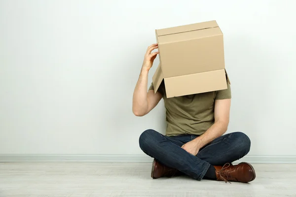 Hombre con caja de cartón en la cabeza sentado en el suelo cerca de la pared —  Fotos de Stock