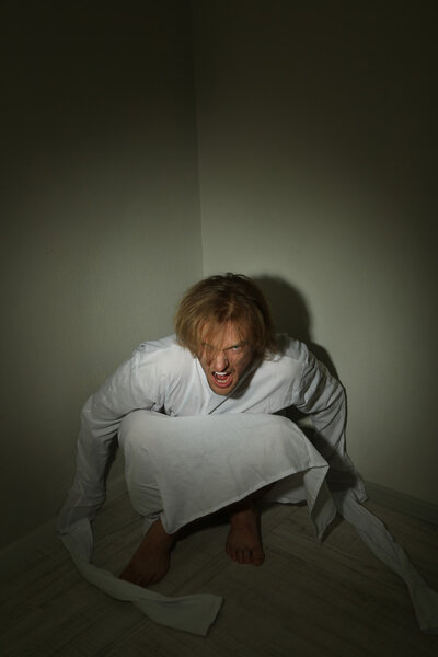 Mentally ill man in strait-jacket in room corner