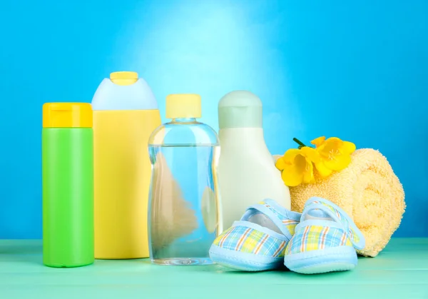 Cosméticos para bebés, toallas y botas sobre mesa de madera, sobre fondo azul — Foto de Stock