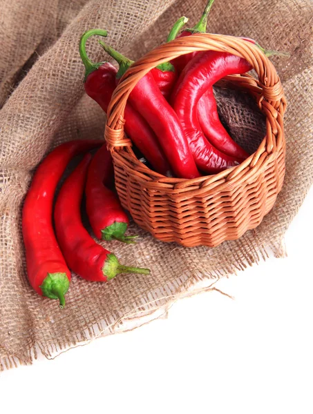 Red hot chili peppers in wicker basket,on sackcloth, isolated on white — Stock Photo, Image