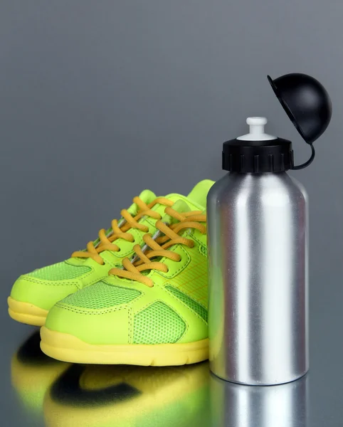 Botella deportiva y zapatillas de deporte sobre fondo gris — Foto de Stock