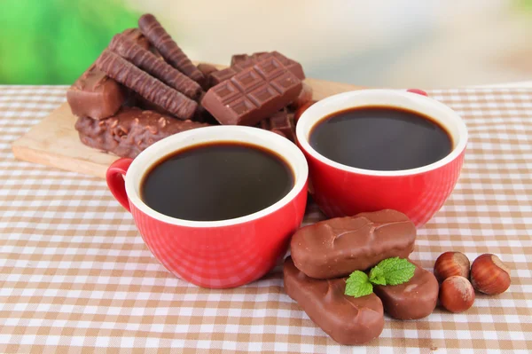 Red cups of strong coffee with chocolate bars on tablecloth on bright background — Stock Photo, Image