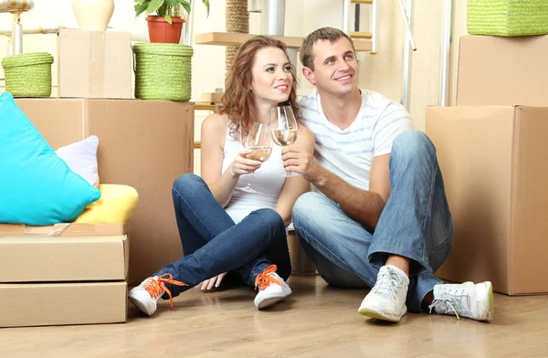 Pareja joven celebrando mudarse a su nuevo hogar sentado entre cajas — Foto de Stock