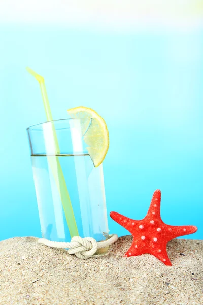 Beach cocktail in sand on blue background — Stock Photo, Image