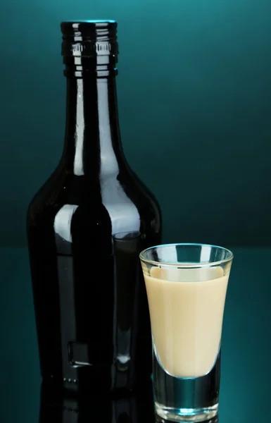 Baileys liqueur in bottle and glass on blue background — Stock Photo, Image