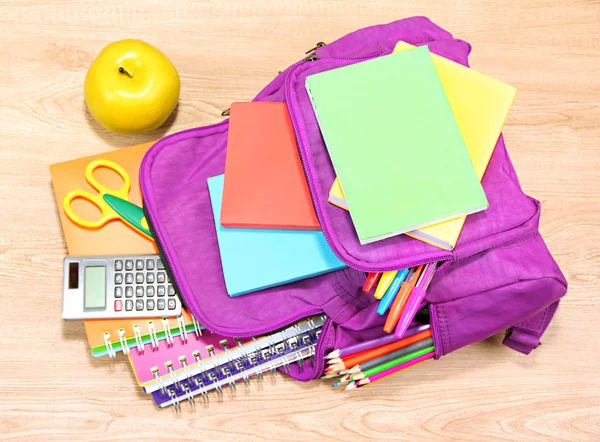 Purple backpack with school supplies on wooden background — Stock Photo, Image