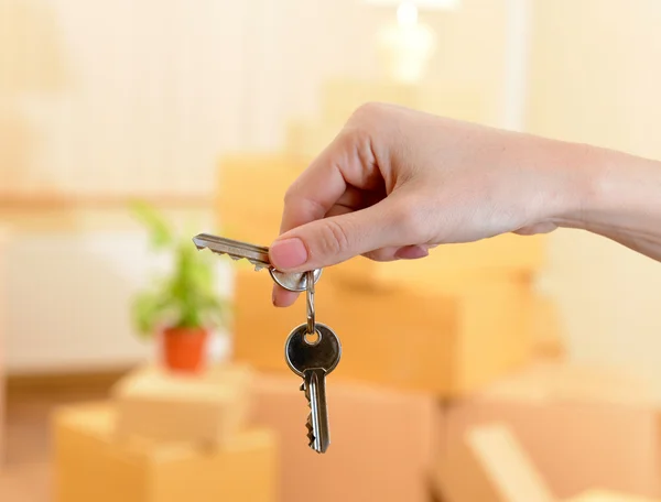 Vrouwelijke hand met sleutels ob stapel kartons achtergrond: bewegende huis concept — Stockfoto