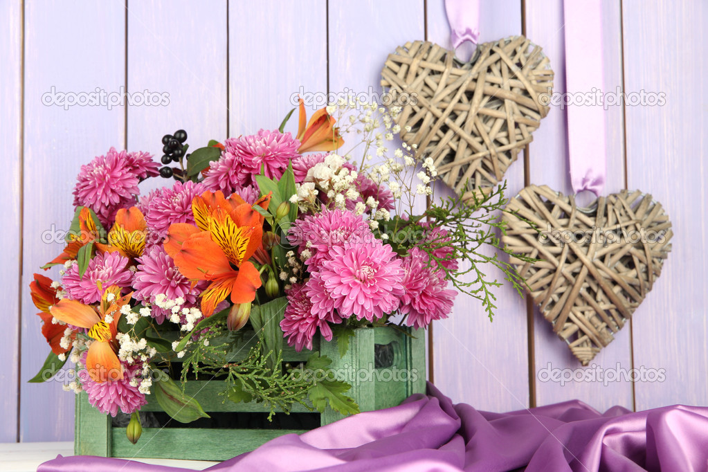 Flowers composition in crate with decorative hearts on table on wooden background