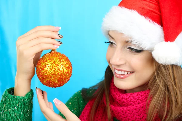 Hermosa chica sonriente con bola de Navidad sobre fondo azul — Foto de Stock