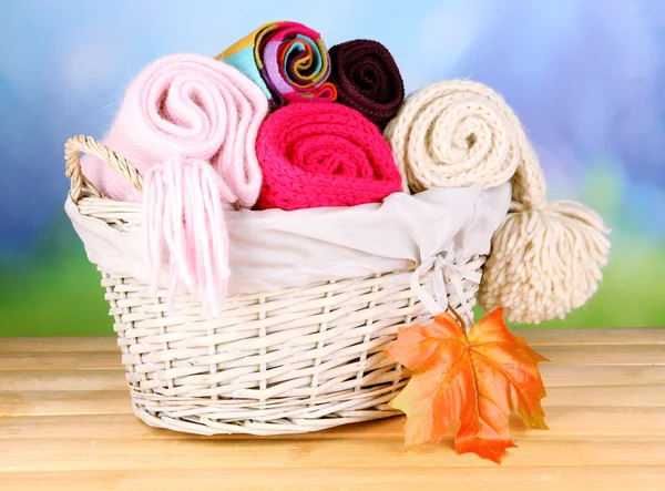 Warm knitted scarves in basket on wooden table on natural background — Stock Photo, Image