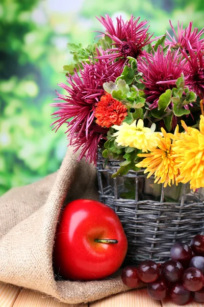 Komposition mit schönen Blumen in Weidenvase und Früchten, auf hellem Hintergrund — Stockfoto
