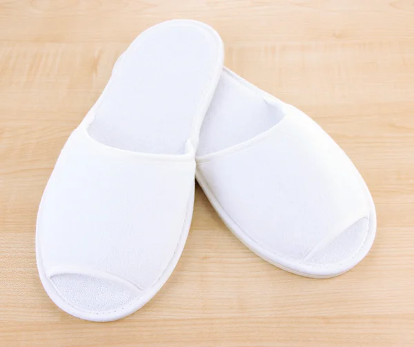 Bílé pantofle na dřevěné pozadí — Stock fotografie