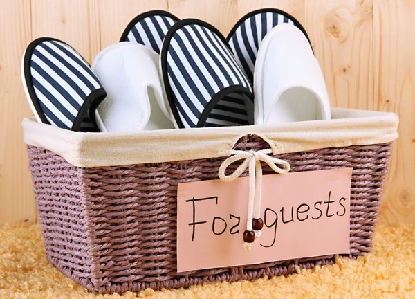 Slippers in basket on carpet on wooden background — Stock Photo, Image