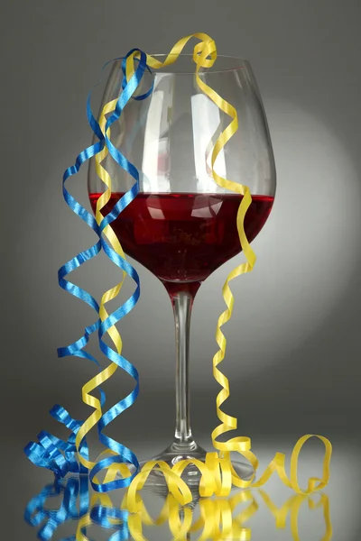 Glass of red wine and streamer after party on gray background — Stock Photo, Image