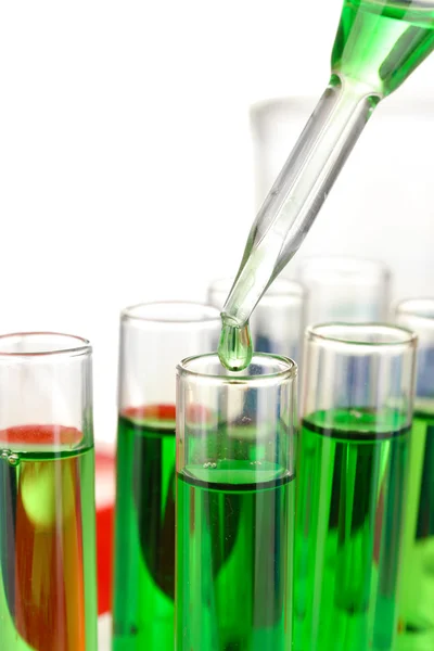 Pipeta de laboratório com gota de líquido de cor sobre tubos de ensaio de vidro, de perto, isolado em branco — Fotografia de Stock