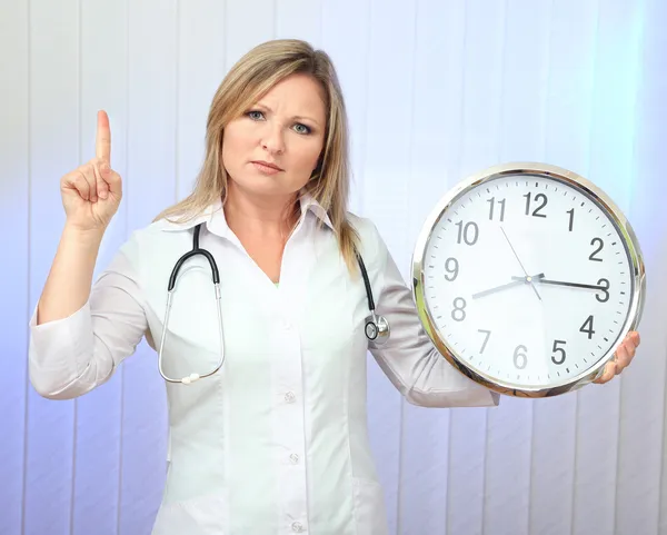 Young beautiful doctor with stethoscope and clock, on light background — Stock Photo, Image