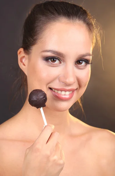 Retrato de una hermosa joven con caramelos de chocolate sobre fondo marrón —  Fotos de Stock