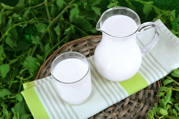 Кувшин и стакан молока на салфетке на плетеном подносе на траве — стоковое фото