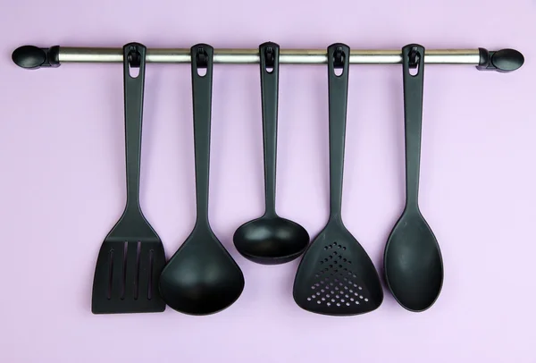 Plastic kitchen utensils on silver hooks on lilac background — Stock Photo, Image