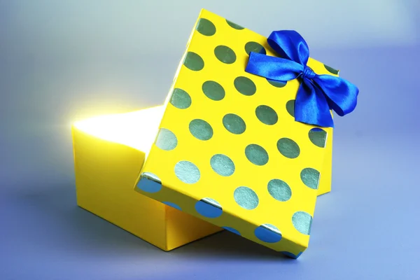 Scatola regalo con luce brillante su di esso su sfondo blu — Foto Stock