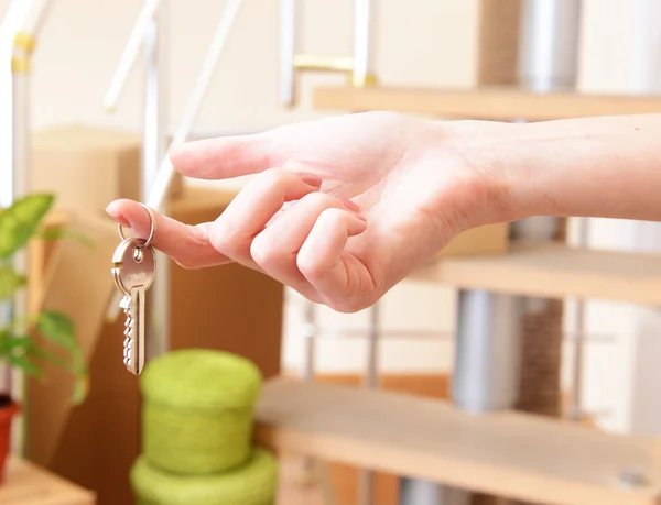 Vrouwelijke hand met sleutels ob stapel kartons achtergrond: bewegende huis concept — Stockfoto