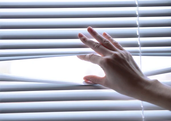 Female hand separating slats of venetian blinds with a finger to see through — Stock Photo, Image