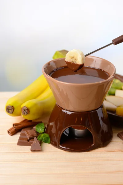Fonduta al cioccolato con frutta, su tavolo di legno, su fondo chiaro — Foto Stock