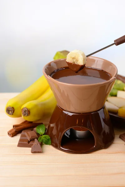 Chocolade fondue met fruit, op houten tafel, op lichte achtergrond — Stockfoto