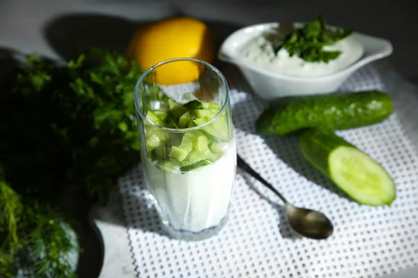 Komkommer yoghurt in glas, op kleur servet, op houten achtergrond — Stockfoto