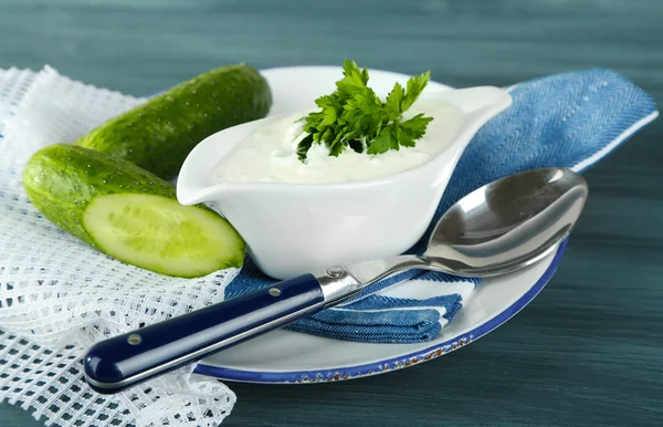 Komkommer yoghurt in sauceboat, op kleur servet, oncolor houten achtergrond — Stockfoto