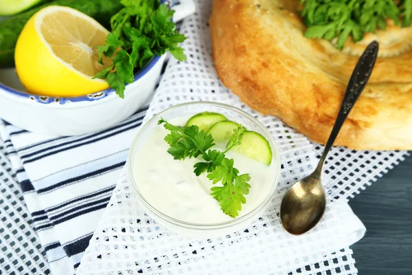 Salatalık yoğurt cam kase ve ev yapımı ekmek, ahşap arka plan üzerinde renkli peçete — Stok fotoğraf