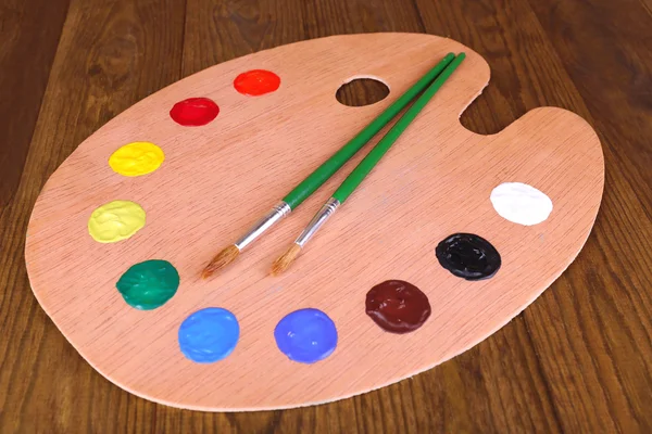 Wooden art palette with paint and brushes on table close-up — Stock Photo, Image