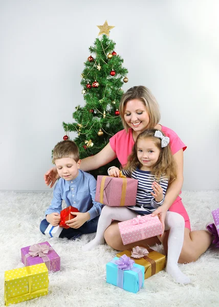 漂亮妈妈和她的孩子与附近装饰圣诞树在房间里的礼物 — 图库照片
