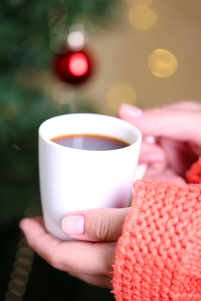 Mãos segurando caneca de bebida quente, close-up, no fundo da árvore de Natal — Fotografia de Stock