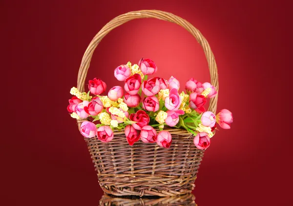 Bouquet of beautiful artificial flowers in wicker basket, on red background — Stock Photo, Image