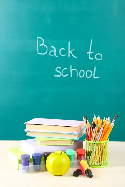 School supplies on table on blackboard background — Stock Photo, Image