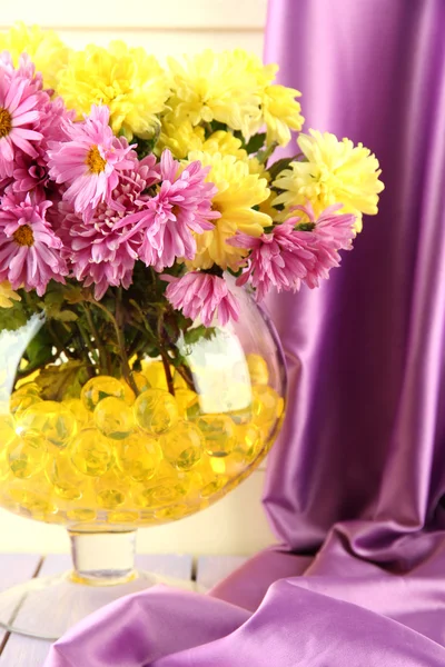 कपड़े पृष्ठभूमि पर टेबल पर हाइड्रोजेल के साथ वाज़ में सुंदर फूल — स्टॉक फ़ोटो, इमेज