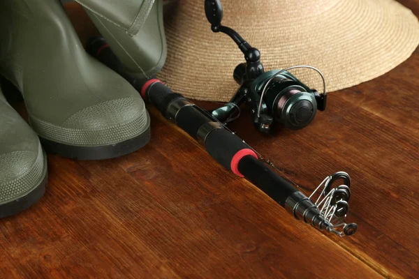Canna da pesca, stivali di gomma e cappello sul tavolo di legno primo piano — Foto Stock
